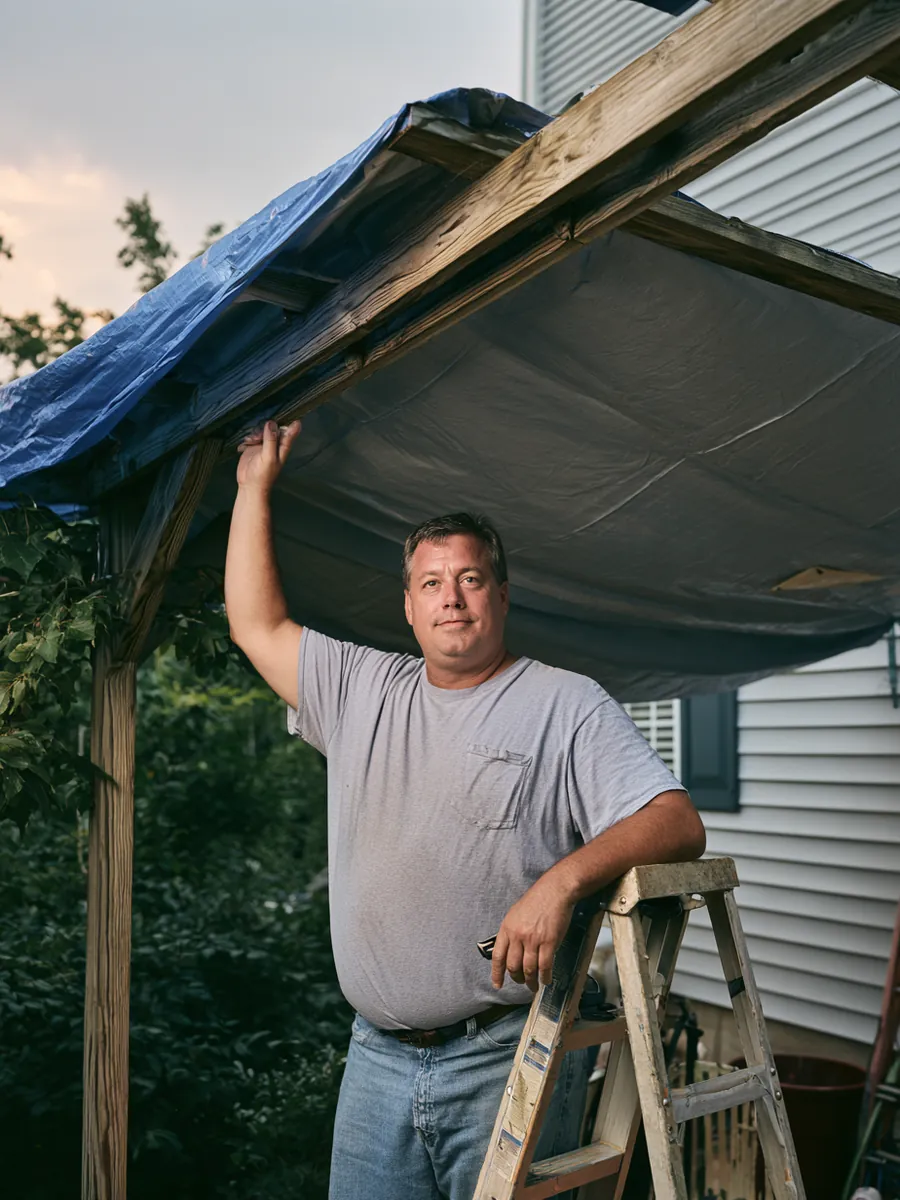 Man securing a tarp over a backyard pergola corner before evening rain, ladder steadied against the beam