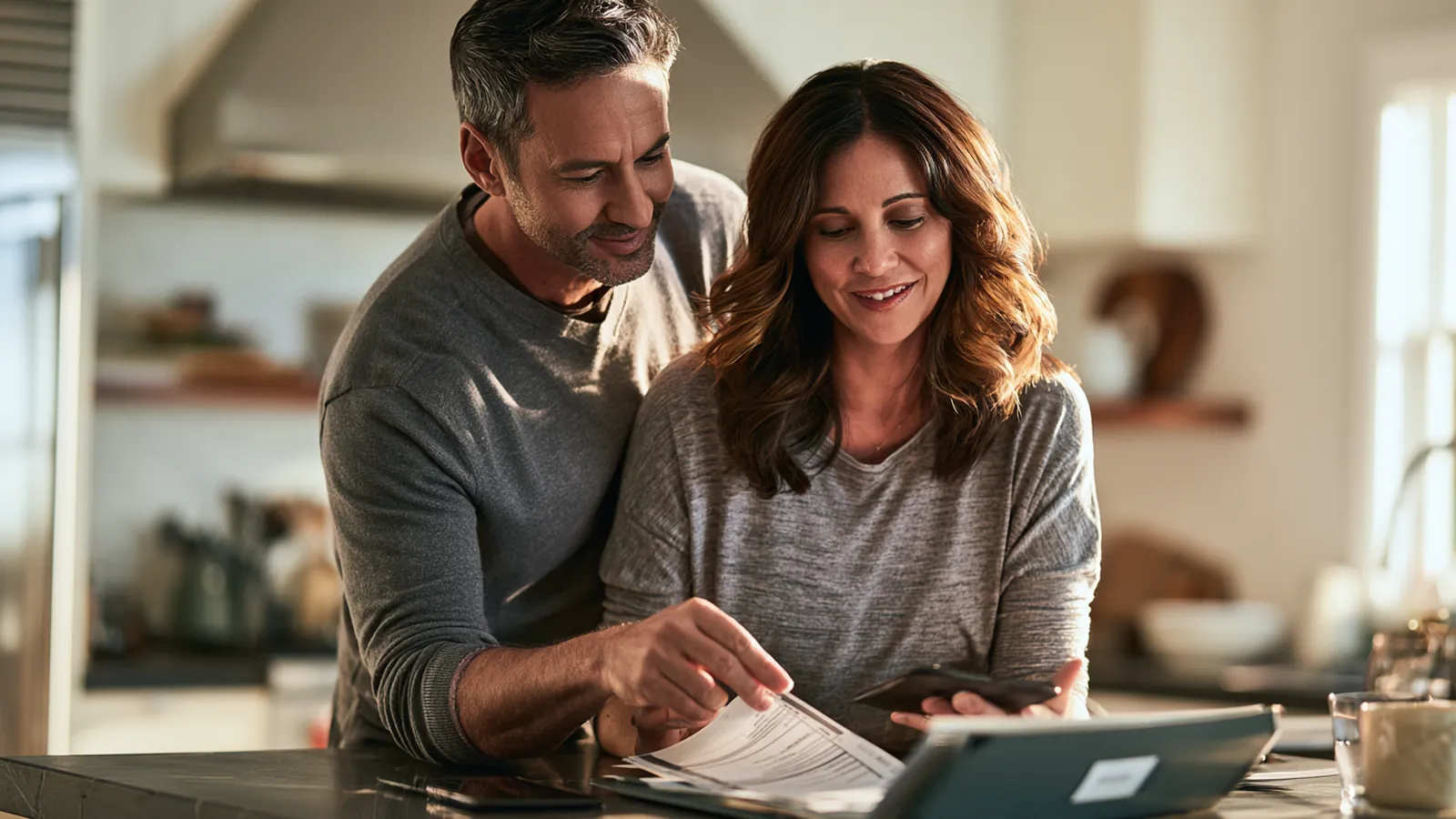 Couple sorting a short stack of statements into one labeled folder on their kitchen island, the first step toward a debt consolidation loan