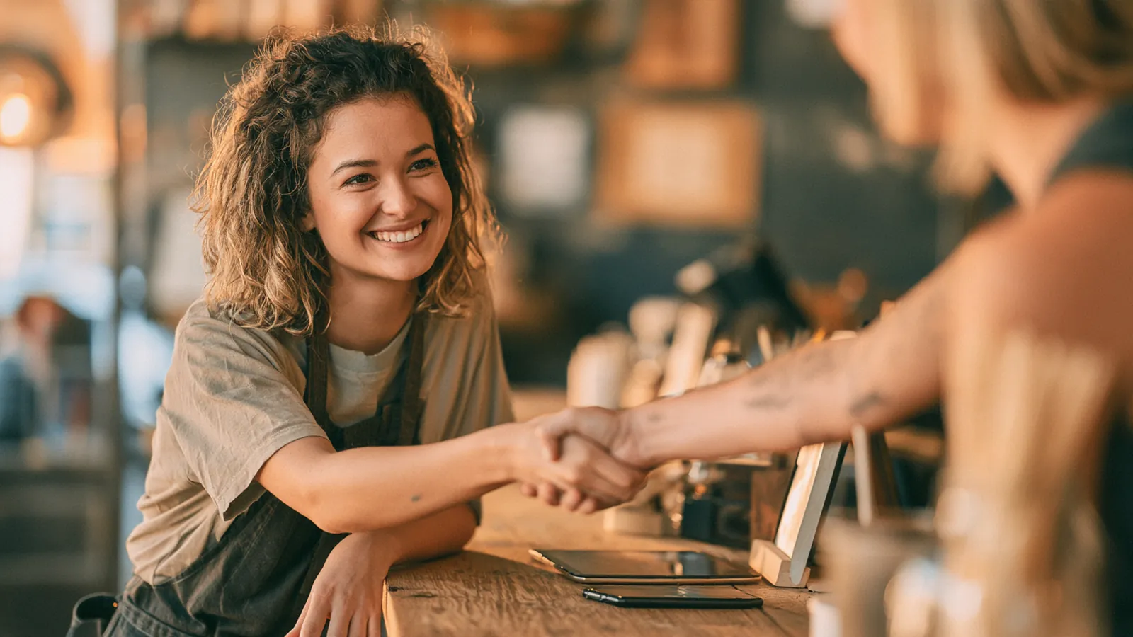 Warm handshake between an advisor and a shop owner across a clean wooden counter, how rise up loans connects borrowers and lenders